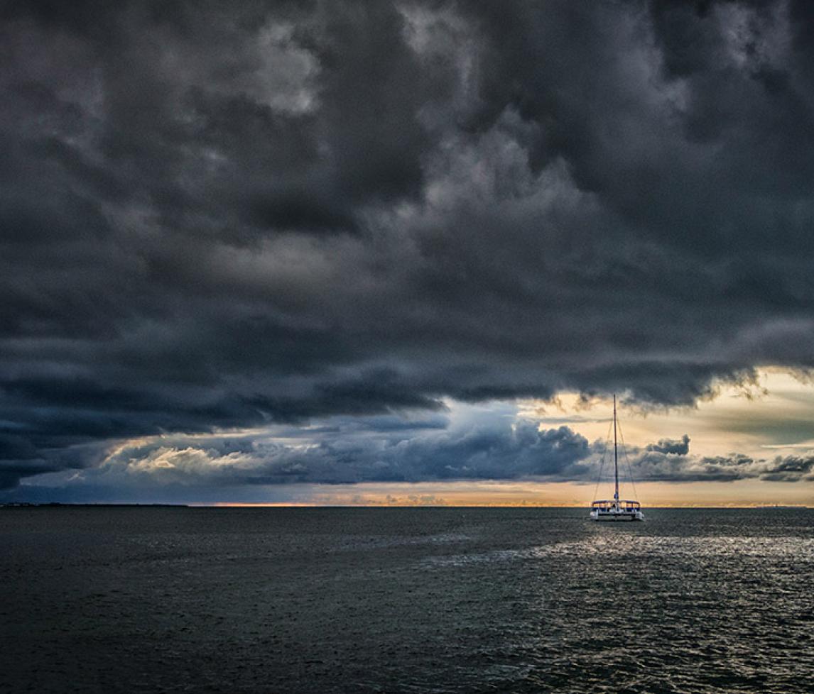 Stormy sky over the sea with a boat in the foreground. Sunlight on the horizon, beyond the storm clouds.