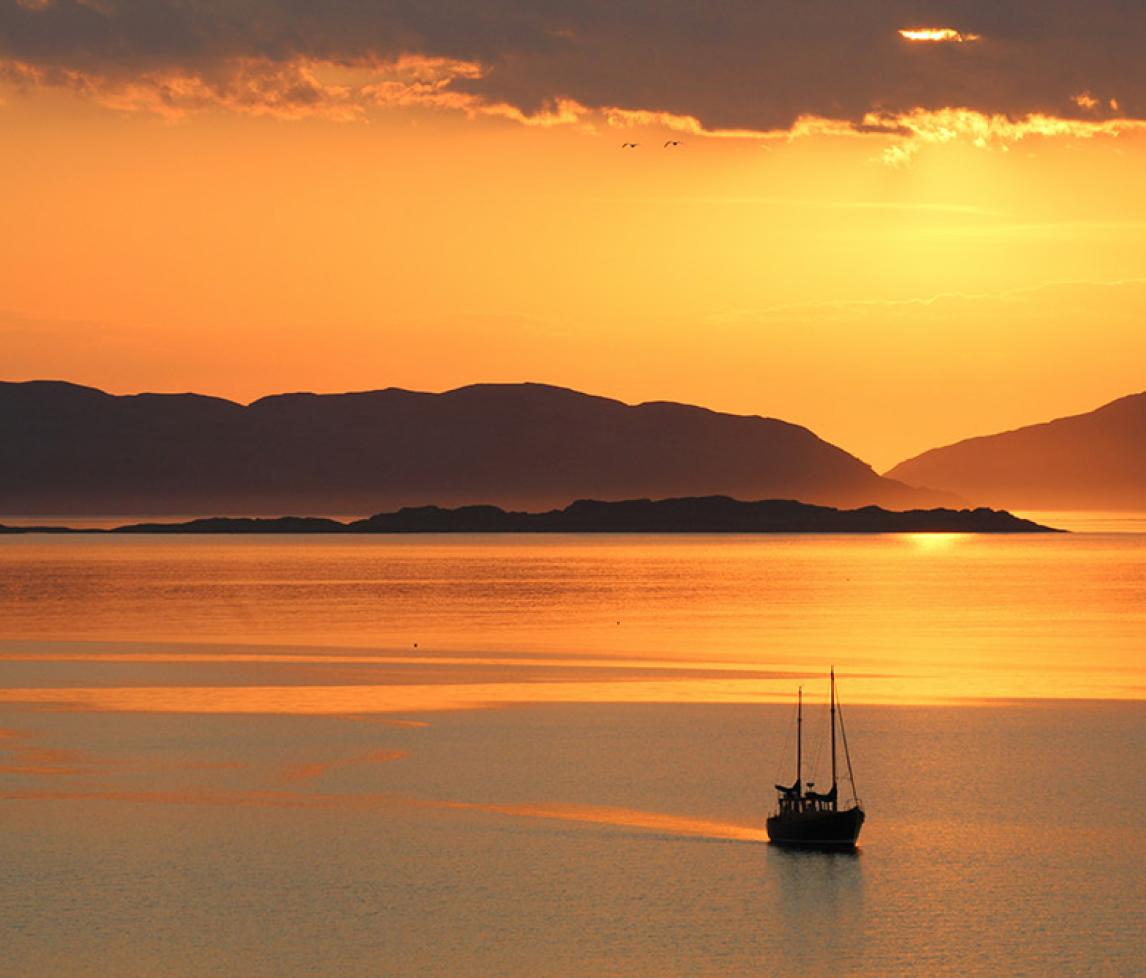 Golden sunset over a body of water with a sailing boat in the foreground